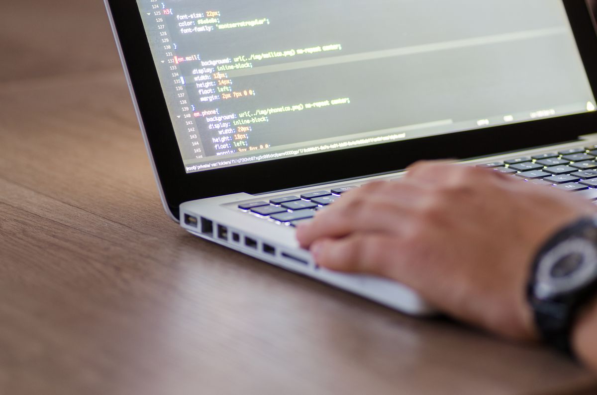 Developer mengetik kode HTML di laptop MacBook Pro